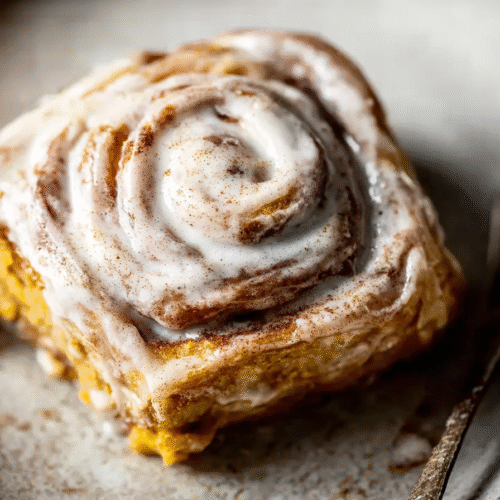 Fluffy pumpkin spice cinnamon rolls topped with cream cheese glaze in a baking pan