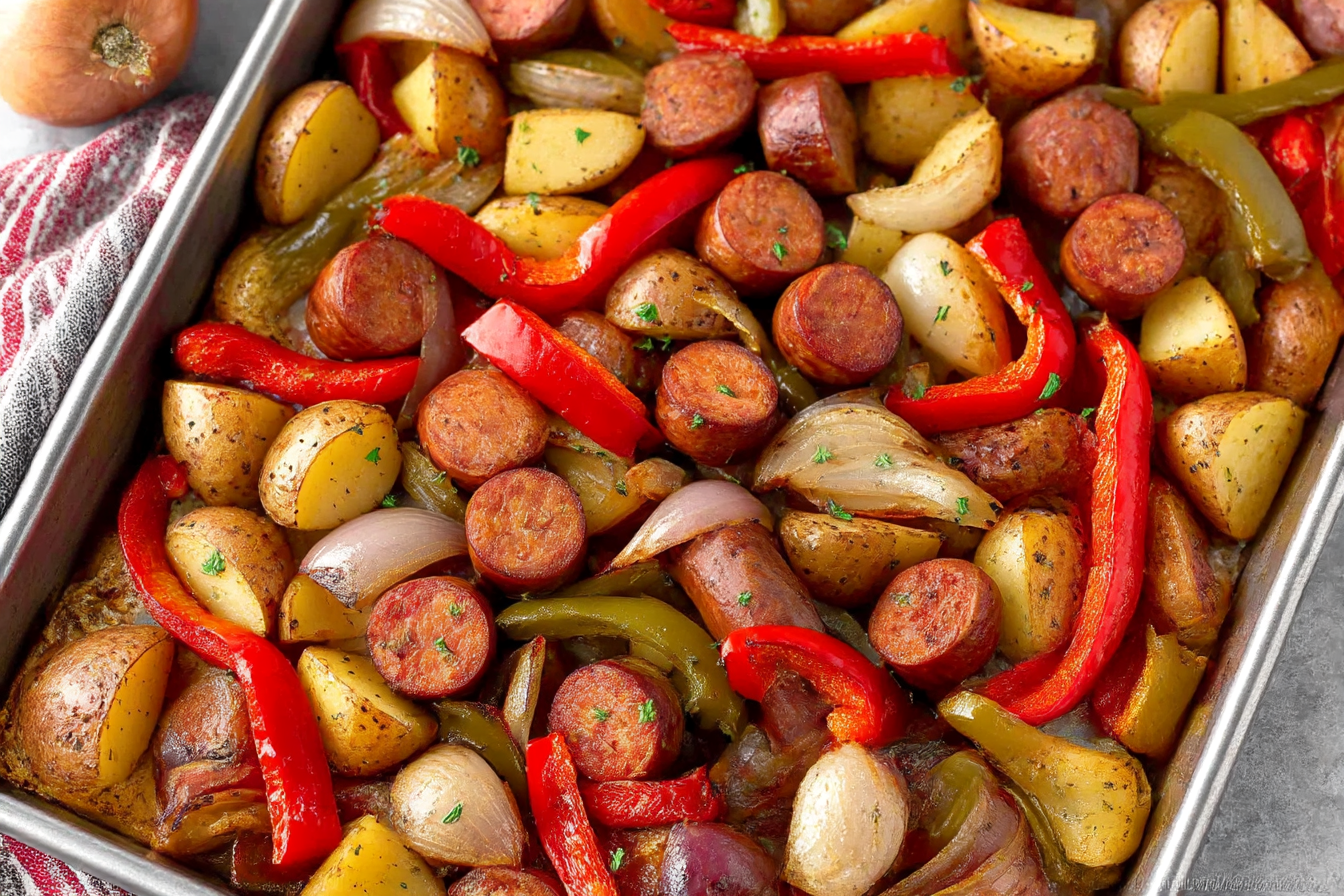 One-pan roasted sausages with peppers, onions, and potatoes on a baking sheet