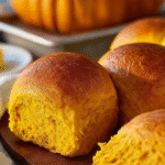 Soft pumpkin dinner rolls with a golden brown crust brushed with butter